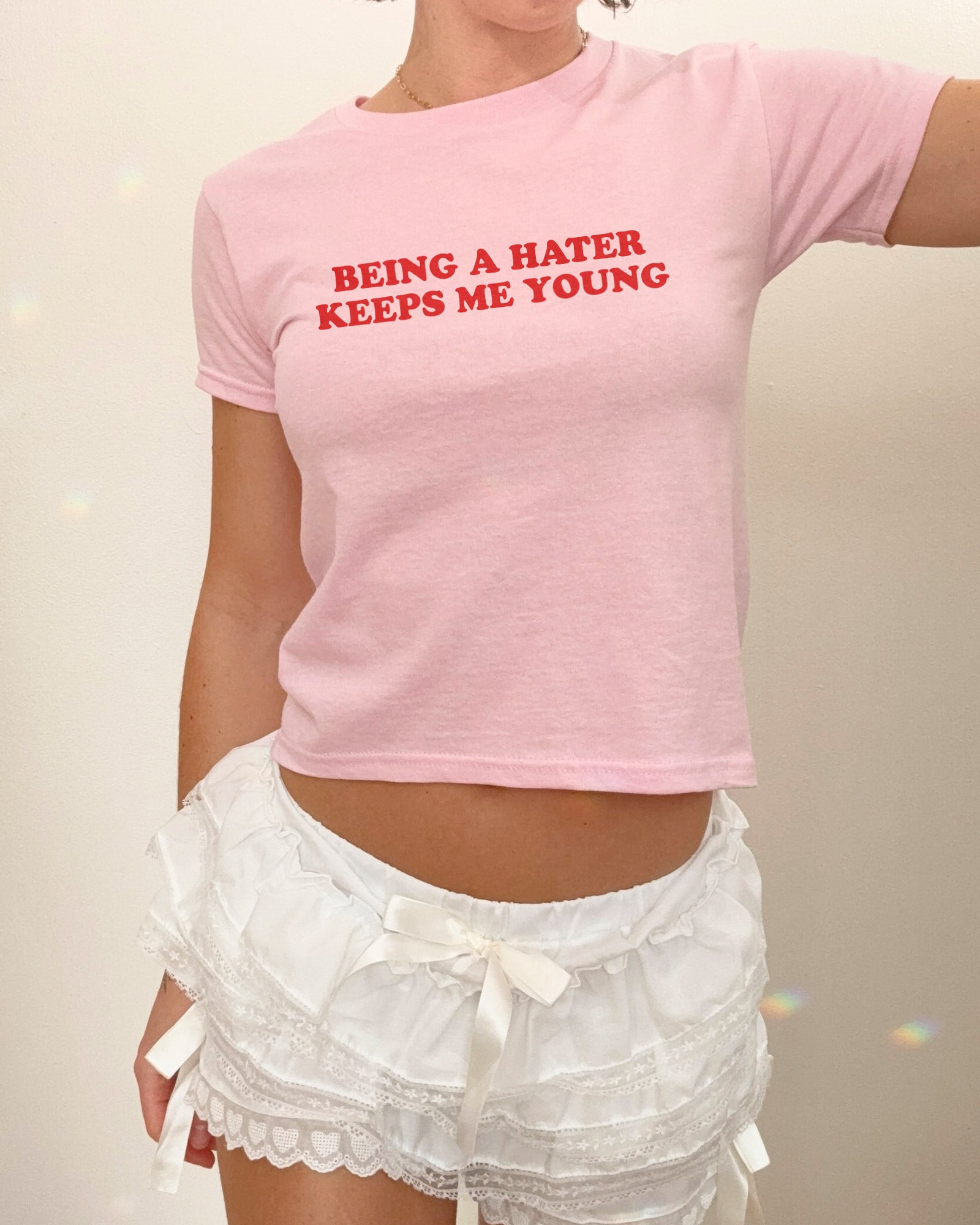 Woman wearing light pink y2k baby tee with funny quote "Being A Hater Keeps Me Young"