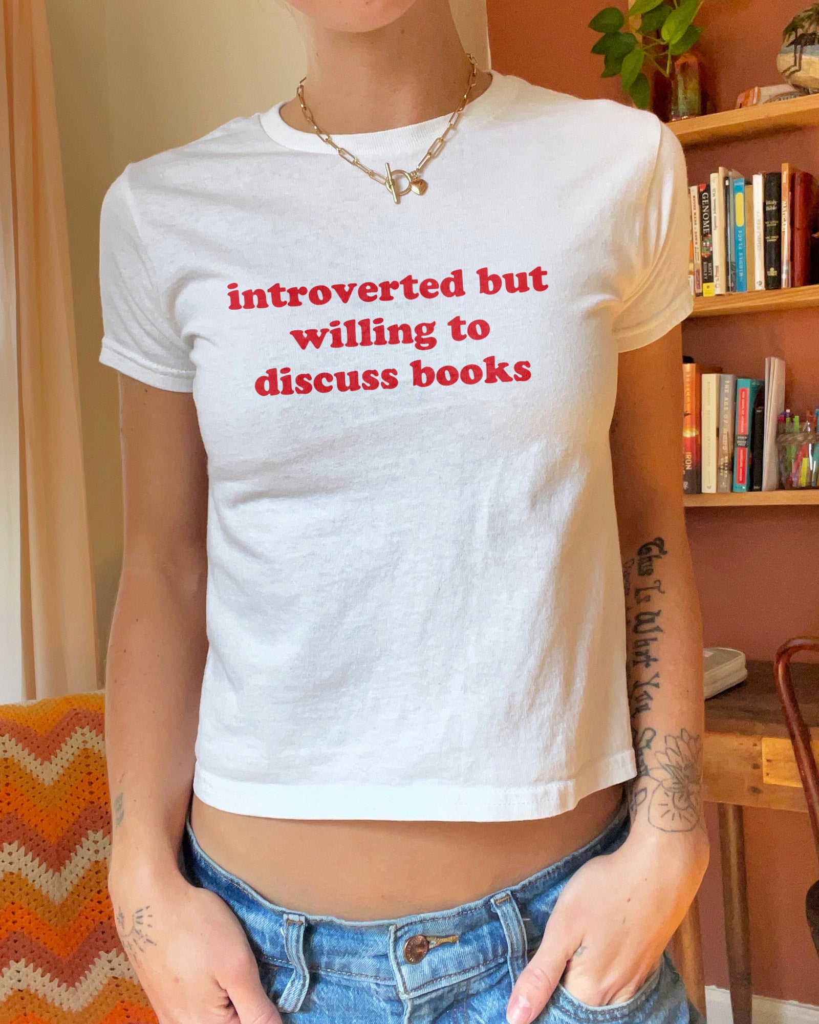 Woman wearing white baby tee with “Introverted But Willing To Discuss Books” quote